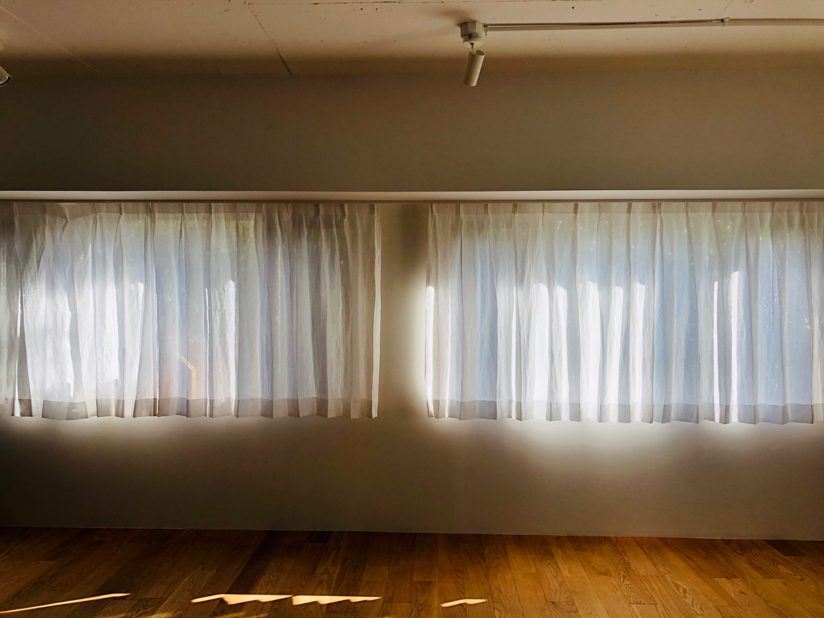 linen curtain　リネットのリネンでお作りしたリネンカーテン事例写真。ル・コルビジェの建築の様な横窓が美しいマンション。内装をリノベーションされ、リネットのリネンカーテンをお選び頂きました。生地は、リビングの窓から、樹々がパノラマ写真の様に見えるという事で、ほんのり景色が見えるぐらいの薄手リネンで。デザインは、カーテンを閉めた時もドレープがある様に、２つ山で。木質系のフローリングと高い天井、シンプルな内装にリネンのカーテンもぴったり納まっています。